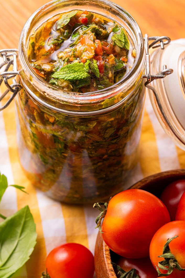 Ce pesto ensoleillé tire ses origines de l’île de Pantelleria au large de la Sicile et se prépare avec certains des plus beaux joyaux de l’été : les fines herbes et les tomates. Vous pouvez bien sûr le préparer à la minute quand l’envie se pointe le bout du nez. Mais on vous encourage fortement à le cuisiner en grande quantité quand la belle saison bat son plein pour garder quelques pots au congélo ou au garde-manger si vous avez opté pour une joyeuse corvée de cannage. En plus de garnir parfaitement toutes vos pâtes préférées, ce pesto peut aussi rehausser vos viandes, poissons, trempettes et bien plus encore.