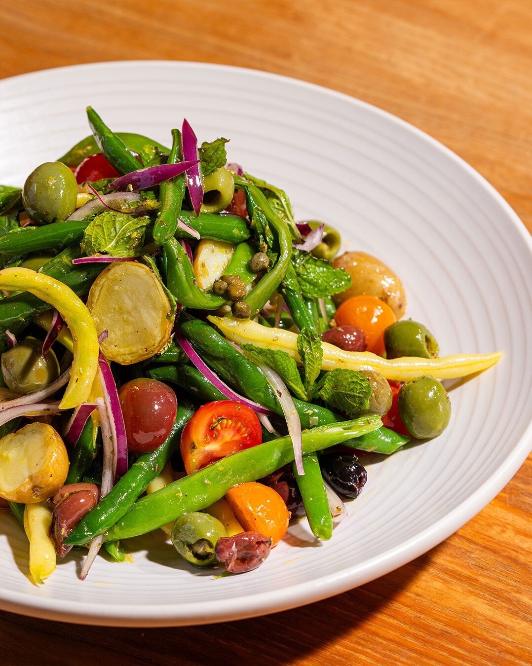 Qu’est-ce que serait un BBQ ou un pique-nique sans salade de pommes de terre? Surtout quand la patate adorée profite d’un traitement sicilien aussi délicieux et coloré! Cette salade qui s’inspire des saveurs phares de la cuisine du sud de l’Italie est composée de pommes de terres, haricots verts, tomates cerises, olives et herbes fraîches. Ce plat est un incontournable à Palerme, sa ville d’origine, mais sa délicieuse simplicité a aussi gagné les cœurs des gens de partout, dont nous. Alors, mettez le cap sur le potager ou le marché et préparez cette superbe salade d’été!