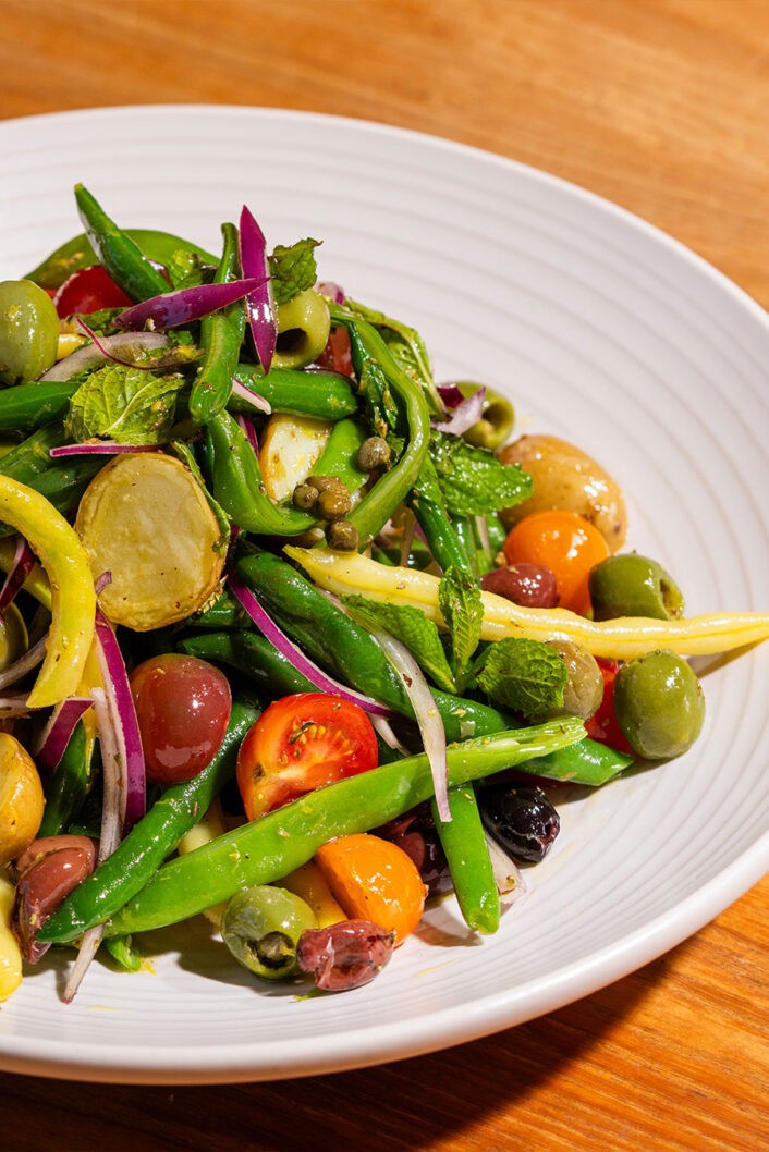 Qu’est-ce que serait un BBQ ou un pique-nique sans salade de pommes de terre? Surtout quand la patate adorée profite d’un traitement sicilien aussi délicieux et coloré! Cette salade qui s’inspire des saveurs phares de la cuisine du sud de l’Italie est composée de pommes de terres, haricots verts, tomates cerises, olives et herbes fraîches. Ce plat est un incontournable à Palerme, sa ville d’origine, mais sa délicieuse simplicité a aussi gagné les cœurs des gens de partout, dont nous. Alors, mettez le cap sur le potager ou le marché et préparez cette superbe salade d’été!